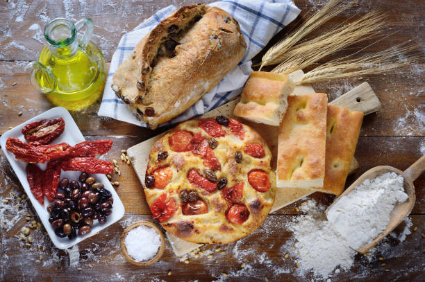 Focaccia with cherry tomatoes and olives, olive bread, white focaccia, dried tomatoes and olives, top view. Focaccia from Bari and other baked goods on rustic wooden table. puglia photos stock pictures, royalty-free photos & images