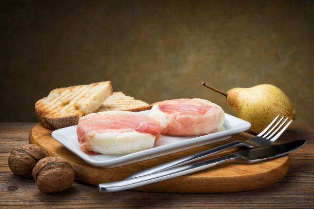 トミーノチーズのスペック(トミーノボスケーオロ)典型的なイタリアのピエモンテチーズ、木製のテーブルにパン、クルミ、梨、コピースペースを焼きます。 - tomino ストックフォトと画像