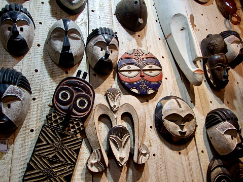 Horizontal closeup of a collection of carved and decorated wooden masks hanging on a wooden wall at the African Craft Market in Capetown
