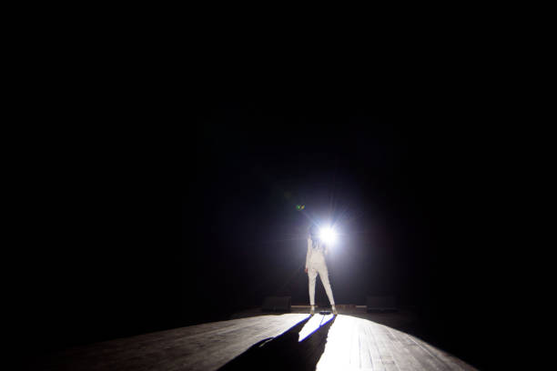 istock Back view of a singer with microphone singing a song on stage in white lights. 1308066213
