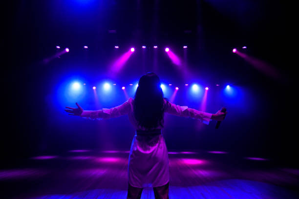 Unrecognizable singer standing on stage at microphone, back view, neon lights unrecognizable singer standing on stage at microphone, back view musical theater stock pictures, royalty-free photos & images