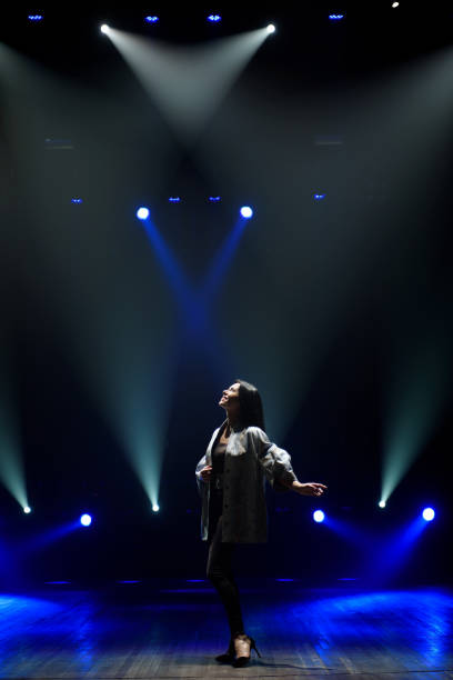 istock Girl in black suit performing on stage with bright blue background 1308066569