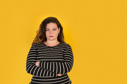 Curvy woman with angry face and crossed arms on a yellow background