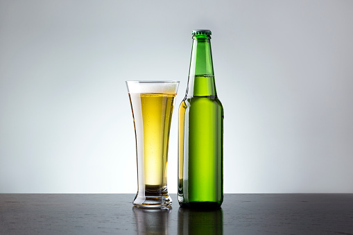 Glass and bottle of fresh beer on grey background. Non alcoholic beer.