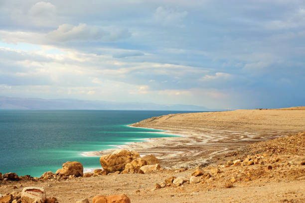 tote sandküste an der jordanseite, trockener sand- und felsenstrand, sonne scheint auf wunderschöner azurblauer wasseroberfläche - hypersaline stock-fotos und bilder