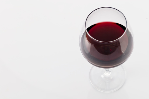 Still-life photography on a white background of a clear glass cup with red wine. The wine creates waves, drops and bubbles inside the glass and is ready to celebrate any event.