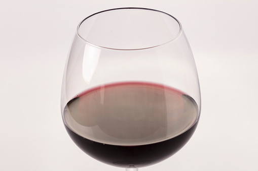 Still-life photography on a white background of a clear glass cup with red wine. The wine creates waves, drops and bubbles inside the glass and is ready to celebrate any event.