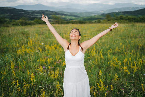 Beautiful young woman in white dress spending relaxing summer day in flower meadow