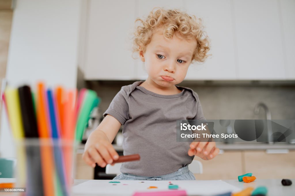 Porträt eines schönen glücklichen Mädchens im Vorschulalter, das an ihrem Küchentisch sitzt und etwas Freizeit genießt. Kleine süße Mädchen macht etwas aus Plastik. Sie macht ein lustiges Gesicht - Lizenzfrei Kinderbetreuung Stock-Foto Porträt eines schönen glücklichen Mädchens im Vorschulalter, das an ihrem Küchentisch sitzt und etwas Freizeit genießt. Kleine süße Mädchen macht etwas aus Plastik. Sie macht ein lustiges Gesicht - Lizenzfrei Kinderbetreuung Stock-Foto