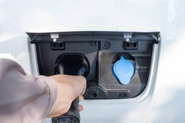 Close up,POV shot, selective focus of a woman's hand grabbing, plugging, holding the EV charger plug handle attached to the socket of electric car. Sustainable energy concept