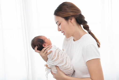 Pretty asian woman smile and holding a newborn baby in her arms. Happy family. Asia mother lifting and looking her adorable infant baby on white. love people concept