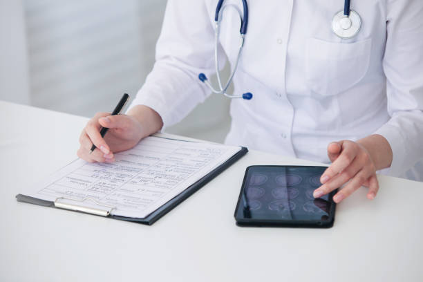 istock Female doctor using tablet and writing diagnosis in medical forms documents 1308089574
