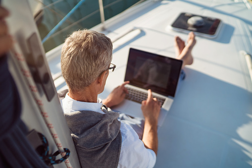Senior man is working during the vacation on a sailboat
