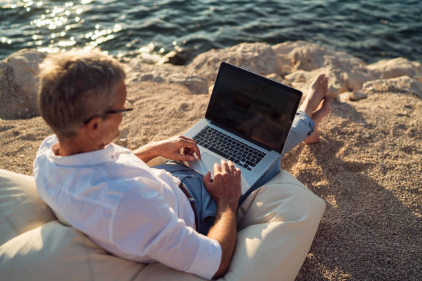 istock Senior man working on his laptop lying on deck chair on the beach 1308090714