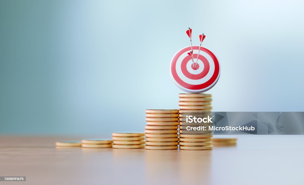 Success And Accuracy Concept - Red Dartboard and Arrows Sitting Before Defocused Background Red dartboard and arrows sitting over coin stacks before defocused background. Horizontal composition with copy space. Success and accuracy concept. Savings Stock Photo