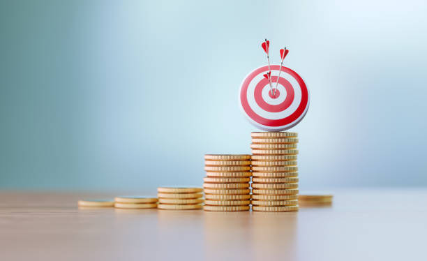 Success And Accuracy Concept - Red Dartboard and Arrows Sitting Before Defocused Background Red dartboard and arrows sitting over coin stacks before defocused background. Horizontal composition with copy space. Success and accuracy concept. super money stock pictures, royalty-free photos & images