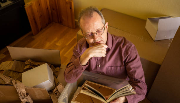 istock Middle aged caucasian man in empty apartment room, reading old diary, unpacking from cardbox boxes for moving house 1308095246