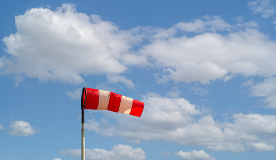 Red and white colored windsock against a cloudy sky. It's a sunny day in the Dutch spring season.