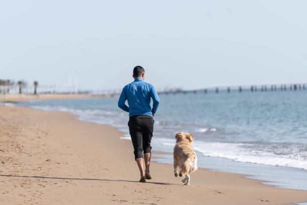 istock Man jogging on the beach with his dog. 1308095548