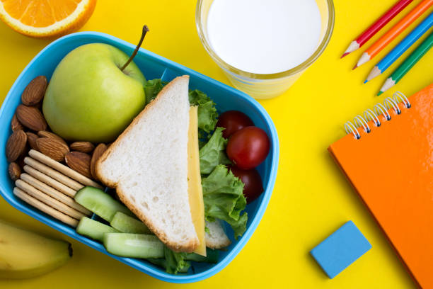 school lunch in the box, milk in the drinking glass and notebook on the yellow background - lunch box lunch red apple imagens e fotografias de stock