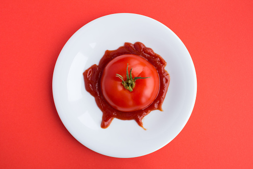 Sliced tomato in ketchup on the white plate on the red background.Top view.Diet minimal concept.