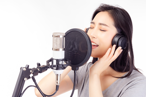 Singer woman singing song in recording studio, using microphone, pop filter and headphones for recording music Singer young female performing and singing in music studio isolated white background