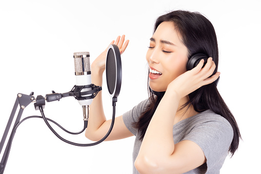 Singer woman singing song in recording studio, using microphone, pop filter and headphones for recording music Young female performing and singing in music studio facial expression, isolated on white