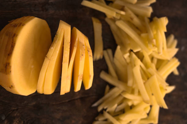 patatas de corte redondo en el medio con un montón de pequeños trozos de papas en rodajas sobre un fondo de madera marrón oscuro aislado en luz natural. - french fries fast food french fries raw raw potato fotografías e imágenes de stock