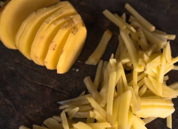 patatas de corte redondo en el medio con un montón de pequeños trozos de papas en rodajas sobre un fondo de madera marrón oscuro aislado en luz natural. - french fries fast food french fries raw raw potato fotografías e imágenes de stock