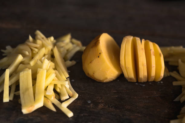 patatas de corte redondo en el medio con un montón de pequeños trozos de papas en rodajas sobre un fondo de madera marrón oscuro aislado en luz natural. - french fries fast food french fries raw raw potato fotografías e imágenes de stock