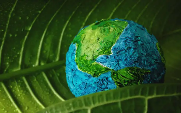 Photo of World Earth Day Concept. Green Moisture Leaf with Droplet Water Embracing a Handmade Globe. Environment to Love and Care