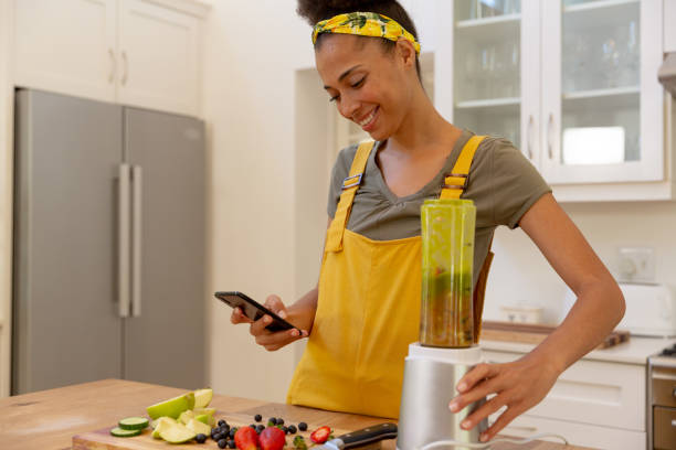 istock Mixed race woman making a healthy drink using smartphone and smiling in a kitchen 1308102630