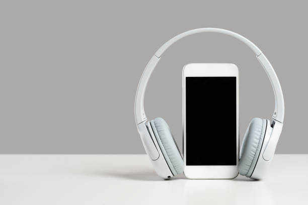 Smartphone mockup display with grey wireless headphones on gray background Smartphone mockup display with grey wireless headphones on white desk gray background. Copy space. Audio technology apps, music podcasts books podcast mobile stock pictures, royalty-free photos & images