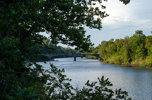A warm sunny day provided a beautiful scenic photograph of a bridge over waters in a Kansas river with lots of green trees.