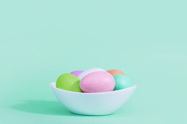 istock Easter background. A collection of Easter eggs in pastel colors in a plate basket on a blue-green background, with harsh shadows and light. 1308112556