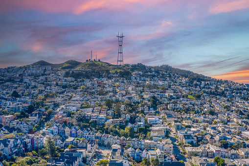 Aerial view of colorful Row Houses in Noe Valley district of San Francisco.\nPastel colored sky casting shadows over the colorful houses and behind Sutro Tower.