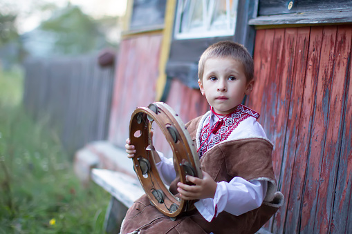Little boy in Slavic national dress with an ethnic tambourine. A Belarusian or Ukrainian child in an embroidered shirt with a folk musical instrument.