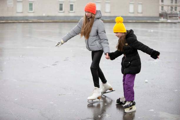 dzieci na łyżwach na lodowisku miasta. starsza siostra uczy młodszego jeździć na łyżwach. - ice skating ice hockey child family zdjęcia i obrazy z banku zdjęć