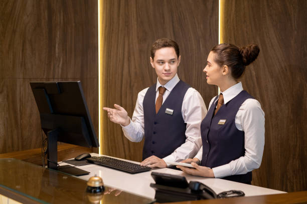 istock Young hotel receptionists looking at colleague with touchpad and pointing at computer screen 1308125719