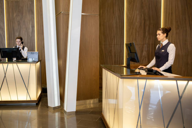 istock Young elegant female receptionist in uniform standing by counter and looking at computer screen 1308125746