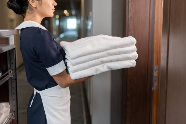 istock Young beautiful chambermaid in uniform holding stack of clean towels while going to enter room 1308125771