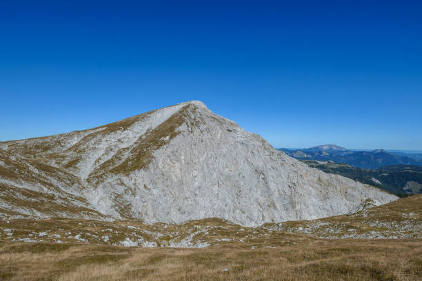 A panoramic view on Hochschwab mountain chains from the pathway leading to Hohe Weichsel. There is a vast pasture on top of a mountain, slowly turning golden. Clear view. Blue sky above. Autumn vibe