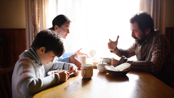 Portrait of poor sad small girl with parents indoors at home, poverty concept. Portrait of poor sad small girl with parents eating indoors at home, poverty concept. family mother poverty sadness stock pictures, royalty-free photos & images