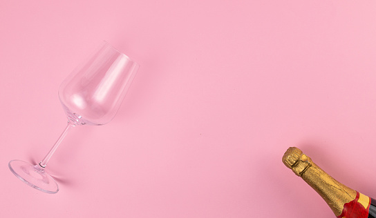 Wine glass and champagne bottle on pink background. Flat lay concept.