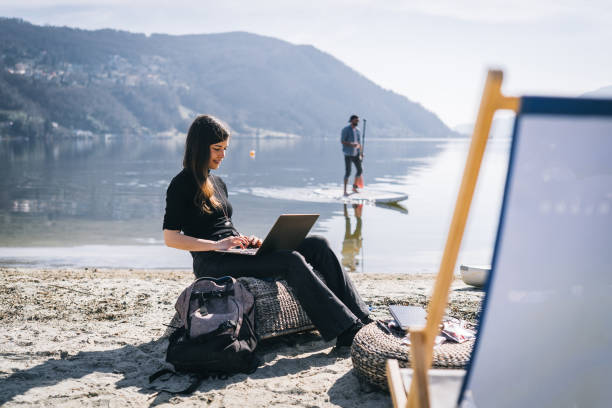 giovane donna lavora su laptop in riva al lago al mattino - paddleboard oar women lake foto e immagini stock