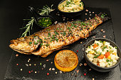 Baked perch fish isolated on blacstand with lemon rosemary and salad