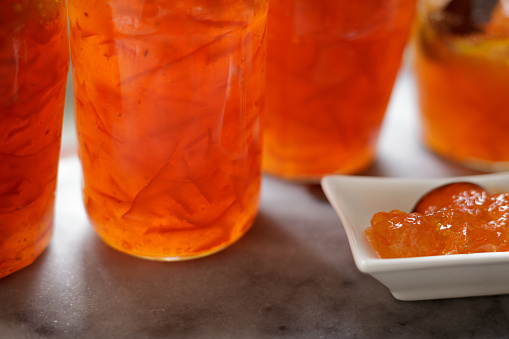 Making a small batch of homemade bitter orange marmalade in a domestic kitchen. Ingredients: Seville oranges (using the whole fruit, including peel and pips), Amalfi lemon juice and pips, preserving sugar, and water. Glass jars and a small porcelain dish with the finished marmalade.