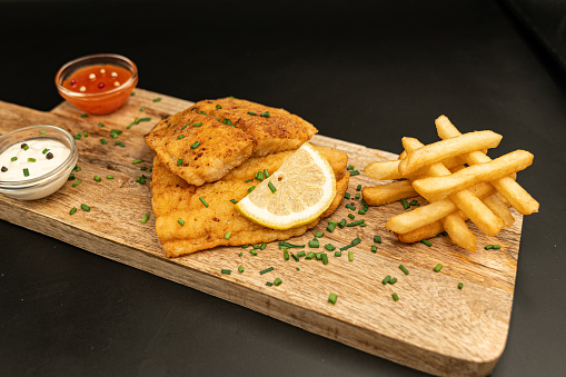 Closeup view of fried breaded fish filets with lemon and pumpkin puree in a metal board on the wooden table.