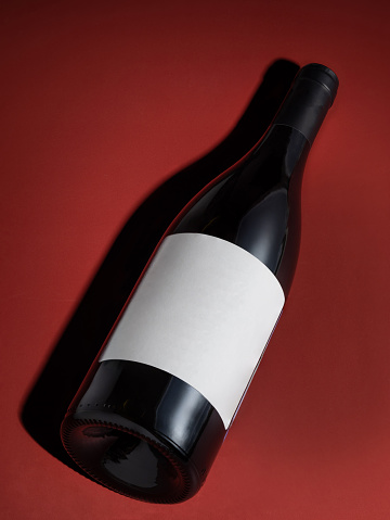 A bottle of red wine on a red background. bottle label without text. Hard shadows. Advertising photography. Red wine. Own winery.