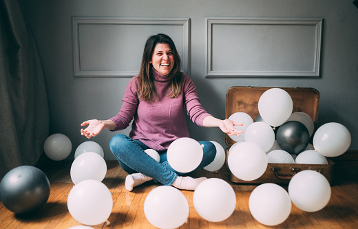 Young woman playing surrounded by balloons over gray background